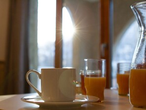 A breakfast setting with a white cup and saucer, a glass of orange juice, and a pitcher of orange juice on a table by a window. - Studio at the slopes, free WIFI, pets allowed (Briançon)