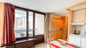 Une cuisine de taille réduite comprenant un coin repas, des meubles de rangement en bois et une fenêtre avec des rideaux.