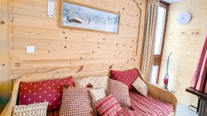 Une pièce chaleureuse aux murs de bois, avec un lit, un tableau représentant un paysage enneigé et une horloge au mur.
