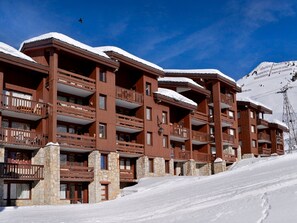 Hotel de vários andares com varandas, alicerces de pedra e paisagem coberta de neve.