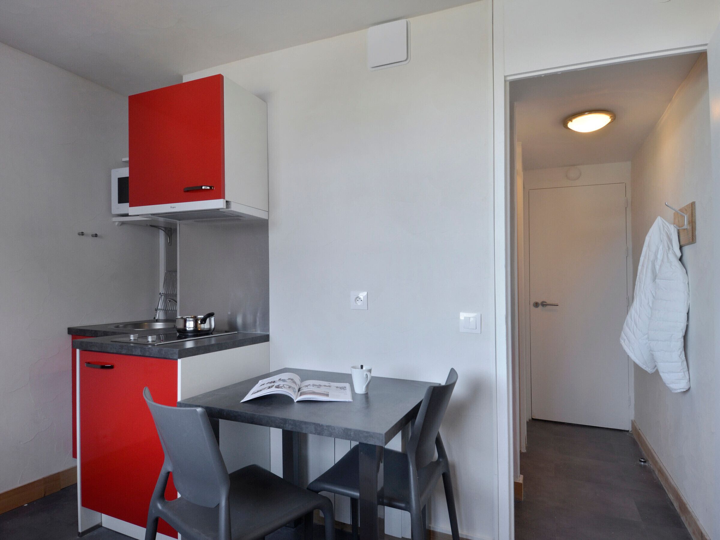 Une cuisine compacte avec un meuble rouge, un micro-ondes blanc et une petite table à manger accompagnée de deux chaises.