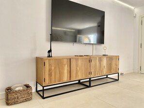A modern living room with a wooden cabinet, a flat-screen TV mounted on the wall, and a woven basket on the floor.