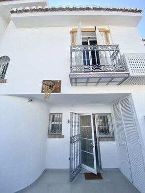 A two-story building with a balcony, a door with a metal gate, and a window with a metal grille.