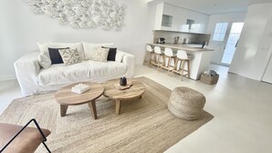 Ein modernes Wohnzimmer mit einem weißen Sofa, einem Couchtisch und einer Küchenzeile mit Barhocker.