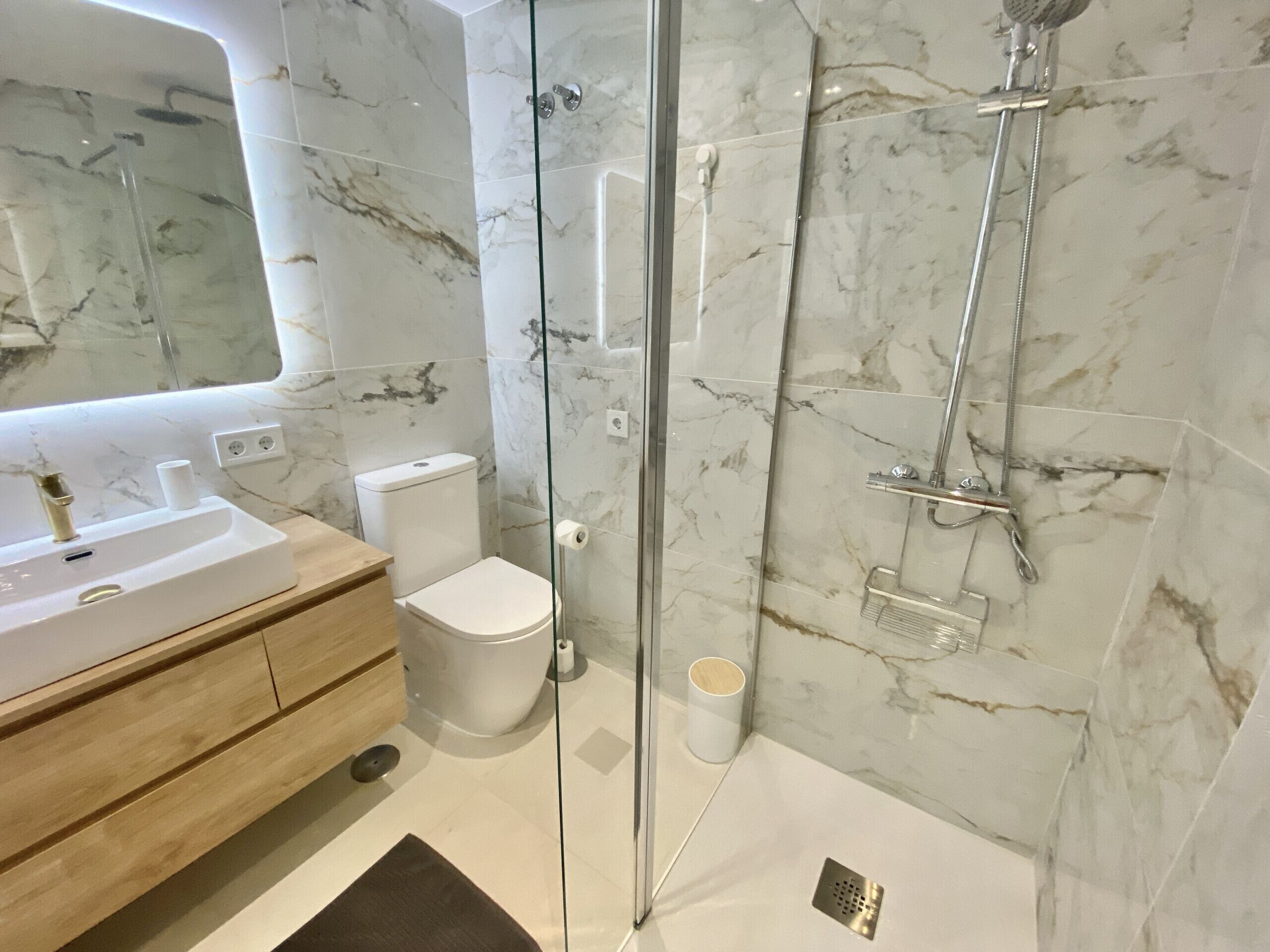 Un baño moderno con ducha de mármol, inodoro y lavamanos.