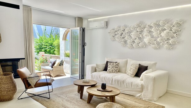 Ein modernes Wohnzimmer mit einer Couch, einem Couchtisch, einem Sessel, einem Kamin und Blick auf Grünflächen.