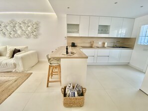 A modern kitchen with white cabinets, a wooden island, and a dining area with a white sofa and a woven basket.