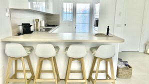 Eine moderne Küche mit einer zentralen Kochinsel, Barhocker und Blick ins Freie durch ein Fenster.