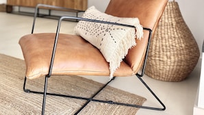 Ein modernes Wohnzimmer mit einer Ledersofa, einem gewebten Pouf und einem Flachbildfernseher auf einem Holzständer.