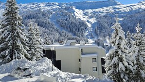 A snow-covered landscape with a building featuring a modern design, surrounded by snow-laden trees and mountains in the background. - Renovated studio 4 people, near slopes, balcony, ski locker (Flaine)