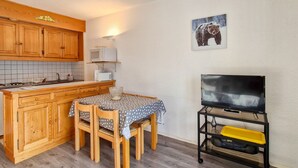 A compact kitchen with wooden cabinets, a microwave, a small dining table with chairs, and a television on a stand. - Renovated studio 4 people, near slopes, balcony, ski locker (Flaine)