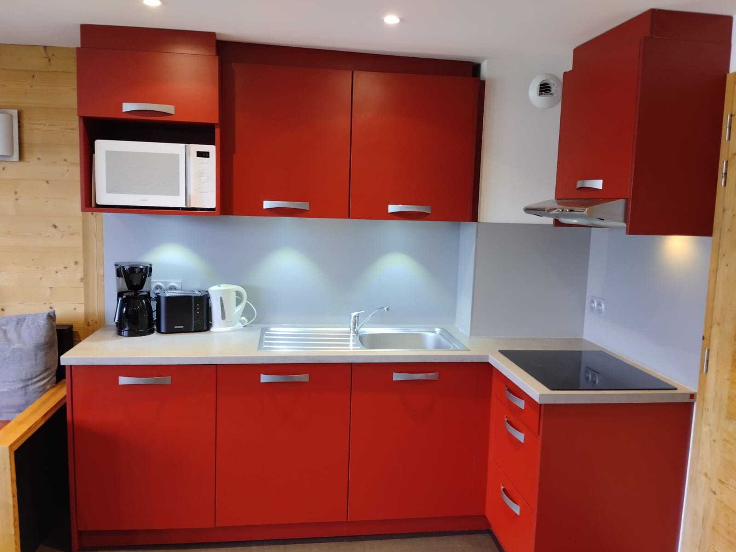 Una cocina compacta con armarios rojos, un microondas blanco, una cafetera y un lavamanos.