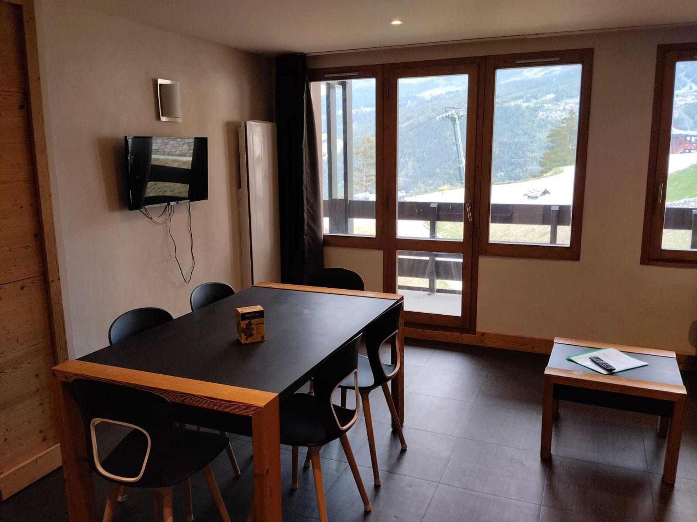 Een vergaderruimte met een grote tafel, stoelen, een aan de muur bevestigde televisie en uitzicht op een bergachtig landschap door de ramen.