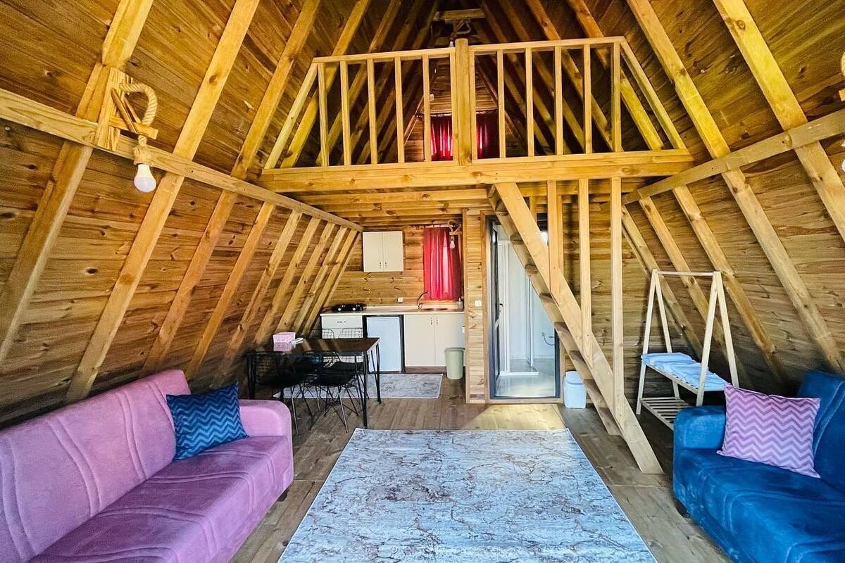 Um quarto estilo sótão com vigas de madeira, cama beliche, uma mesa de jantar e dois sofás.