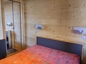 A room with a bed, a wooden wall, a glass door, and a small white object on the wall. - Bright Apartment 5p · Wellness Area · Pets Allowed (La Plagne Montchavin Les Coches)