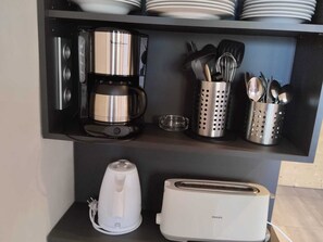 En kökshylla med en kaffebryggare, en brödrost och förvaringskärl för köksredskap.