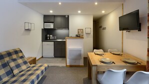 Un espace de vie compact comprenant un coin cuisine, un coin repas et un téléviseur fixé au mur.