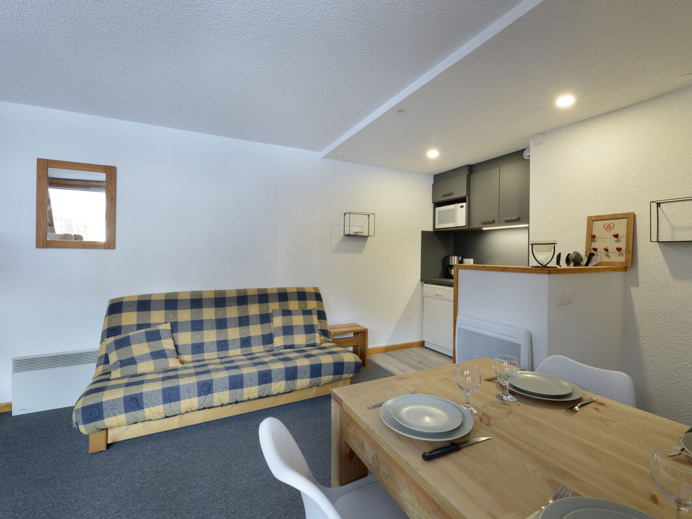 A compact room with a checkered sofa, a dining table set with plates and cutlery, a microwave, and a small cabinet.