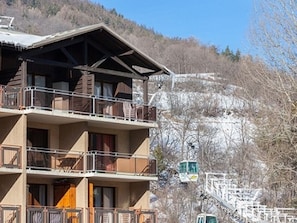 A multi-story building with balconies, a ski lift in the background, and a mountainous landscape.