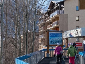 A pedestrian bridge with a metal railing, a building with balconies, and a signboard.