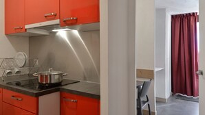 Une cuisine de taille réduite avec des meubles de couleur rouge, une hotte de cuisine en acier inoxydable et une casserole sur la cuisinière.