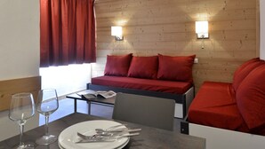 Une chambre d’hôtel avec une tête de lit en bois, deux oreillers rouges, une petite table avec une assiette, des couverts et des verres à vin.