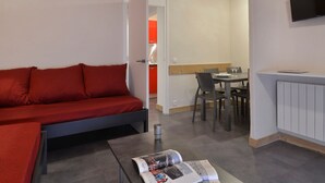 Un espace de vie compact comprenant un canapé rouge, une table à manger avec des chaises et un téléviseur à écran plat fixé au mur.