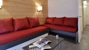 Une pièce moderne avec un mur en bois, un canapé, une table basse avec un magazine et une porte visible au fond.