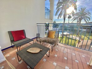 Un balcon avec deux fauteuils en osier, une petite table et un coussin rouge.