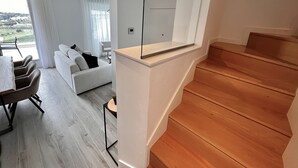 En moderne stue med en hvid sofa, et spiseområde med bord og stole, samt en trætrap.