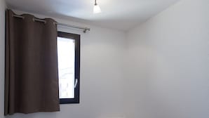 A small, single-room with two single beds, a window with a curtain, and a ceiling light. - Renovated apartment near slopes with Wifi and pets allowed (Briançon)