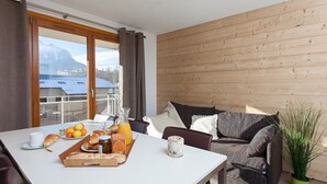 A modern room with a wooden wall, a dining table with breakfast items, a sofa, and a view of mountains through a large window. - Renovated apartment near slopes with Wifi and pets allowed (Briançon)
