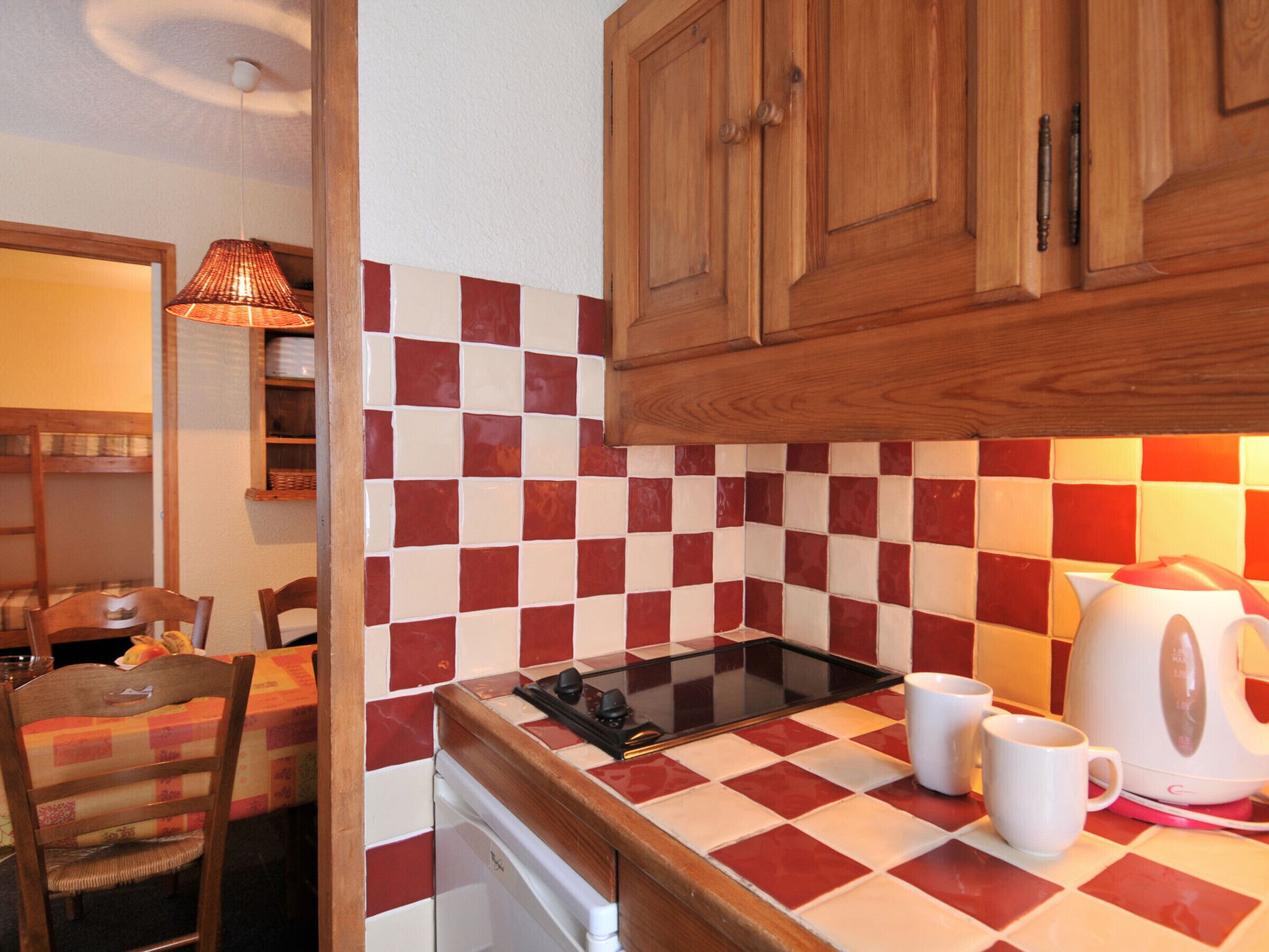 Een keuken met een betegelde achterwand in ruitpatroon, houten kastjes, een fornuis en een waterkoker.