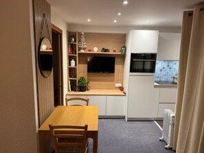 A compact kitchen with a dining area, a built-in TV, and a radiator.