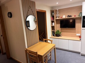 A modern kitchen with a wooden dining table, a built-in TV, and a potted plant.