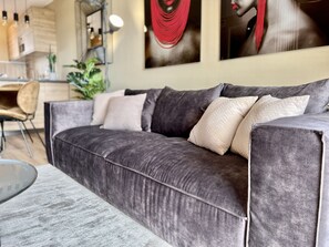 Una sala de estar moderna con un sofá gris, una mesita redonda y un comedor al fondo.