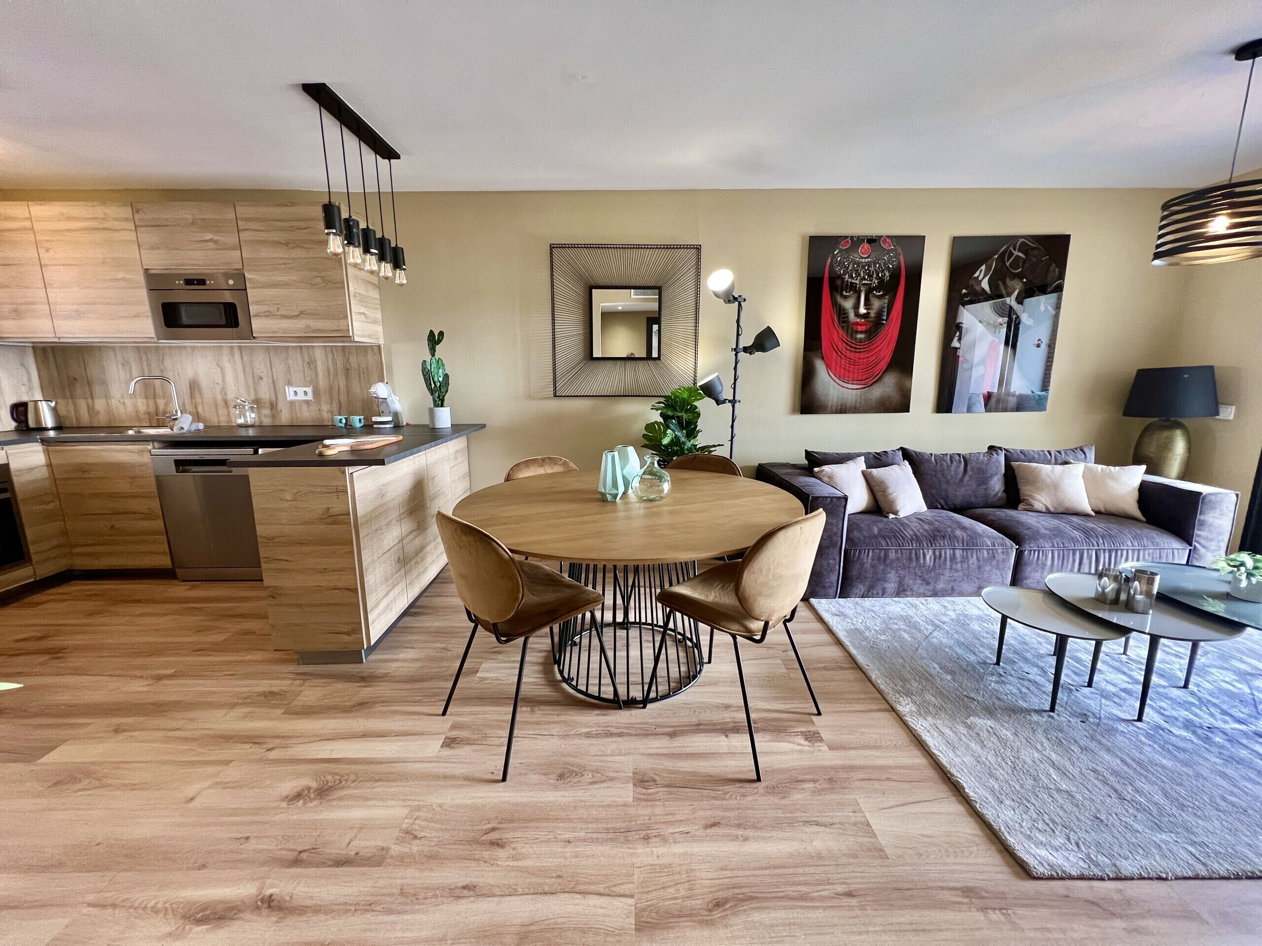 Een moderne keuken met houten kastjes, een ingebouwde oven en een eethoek met een ronde tafel en stoelen.