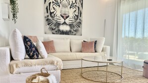 A modern living room with a white sofa, a round coffee table, and a large tiger painting on the wall. - 54 - Apartment on the cala golf course (La Cala de Mijas)