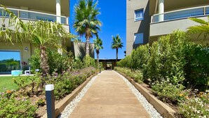 A pathway leading to a building with a modern design, surrounded by lush greenery and palm trees. - 54 - Apartment on the cala golf course (La Cala de Mijas)