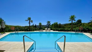 A clear blue swimming pool with a tiled deck, surrounded by palm trees and a clear sky. - 54 - Apartment on the cala golf course (La Cala de Mijas)