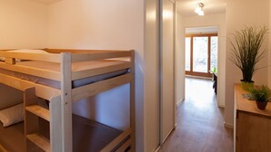 Une chambre avec un lit superposé, une porte coulissante donnant sur un couloir et une plante en pot posée sur une table en bois.