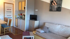 Um espaço compacto com cozinha compacta, sofá, mesa de jantar com cadeiras e uma pequena TV sobre um móvel.