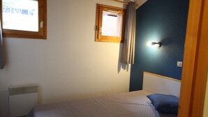 Quarto pequeno com cama de solteiro, janela, radiador e parede azul.