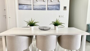 A modern dining area with a white table, three grey chairs, two potted plants, and a black wire basket. - 55 - Apartment in La Cala de Mijas (La Cala de Mijas)
