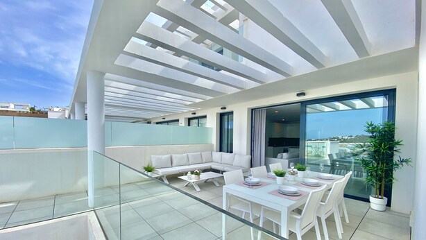 A modern rooftop terrace with a glass balustrade, a white sofa set, a dining table with chairs, and a potted plant. - 55 - Apartment in La Cala de Mijas (La Cala de Mijas)