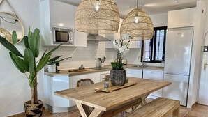 Una cocina moderna con armarios blancos, una mesa de comedor de madera, un banco y una planta grande en maceta.