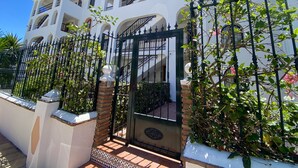 Un edificio de varios pisos con fachada blanca, balcones y entrada protegida por una reja.
