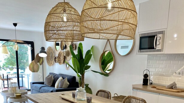 Una cocina moderna con una mesa de comedor de madera, dos lámparas de mimbre colgantes y una planta grande en maceta.