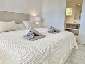 Ein ordentlich bezogenes Bett mit aufgerollten Handtüchern und einer weißen, strukturierten Tagesdecke.