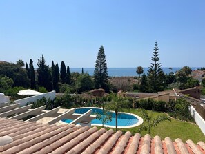 Eine Dachterrasse mit Swimmingpool, Blick auf das Meer und umliegendes Grün.